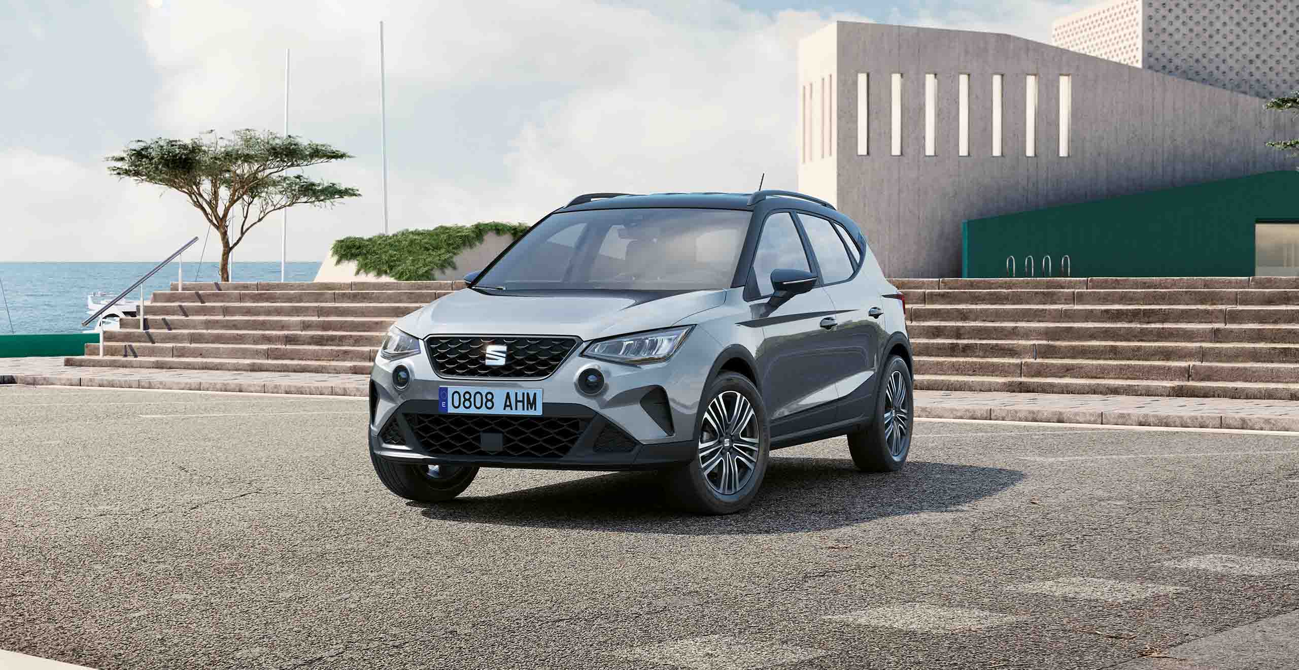 Light blue SEAT Arona 2024 business car crossover SUV parked in sunshine, trees and sea