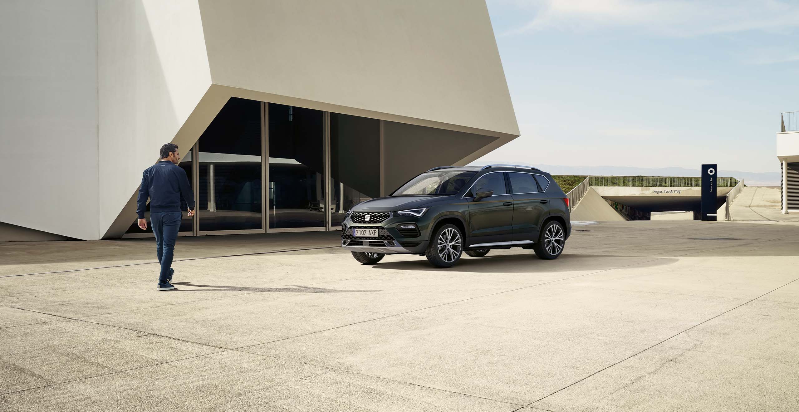 Far away view of man standing by the seat ateca 2024 business car and a concrete building