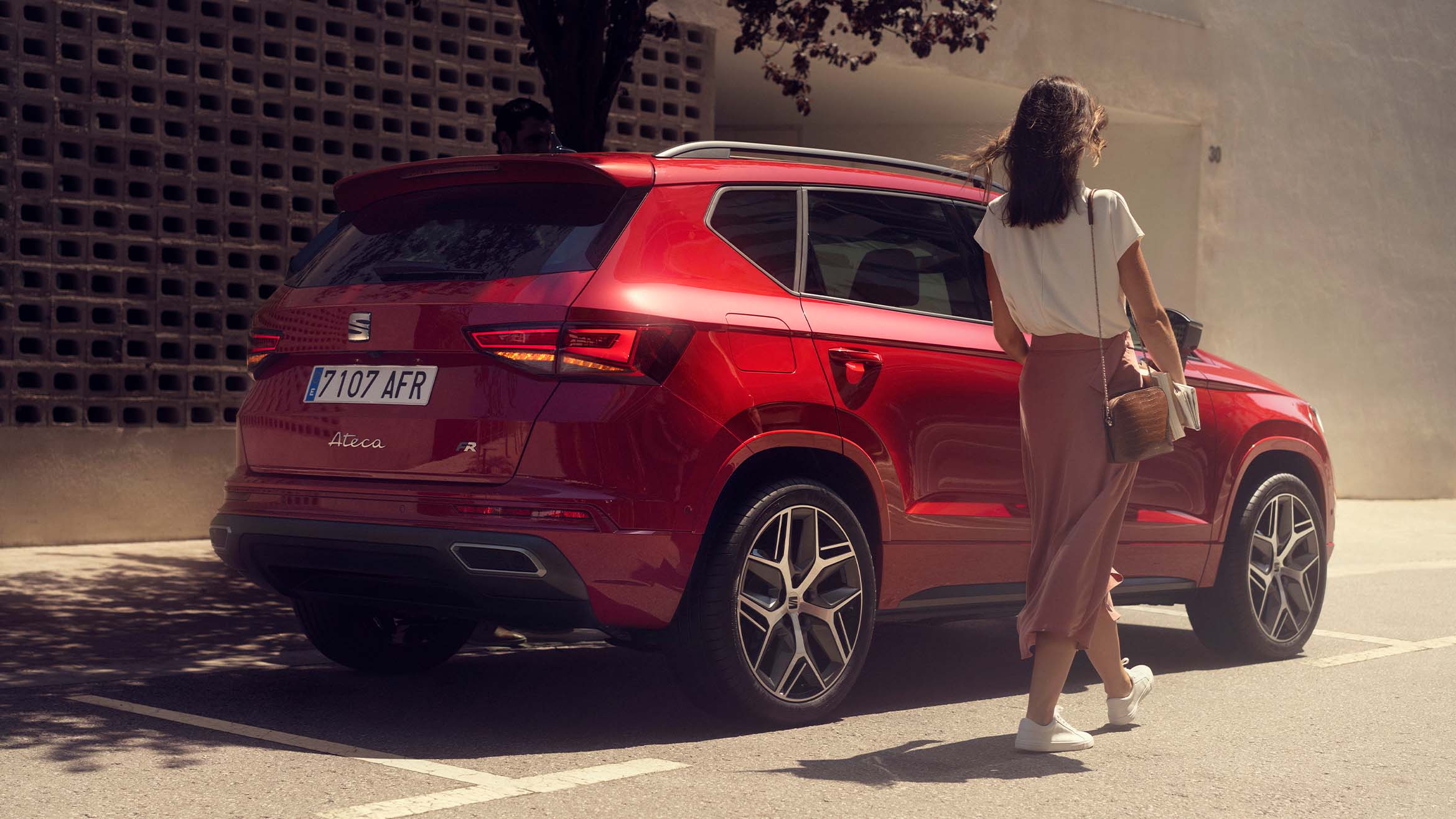 A woman walking next to a Seat Ateca in velvet red colour