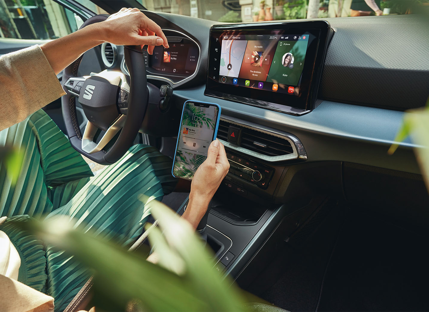 Driver with one hand on the steering wheel while using their smartphone to install OTA updates for SEAT Arona's infotainment system