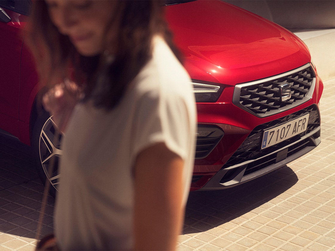 nose of a red seat ateca parked in a sunny spot. A woman is standing next to the car.