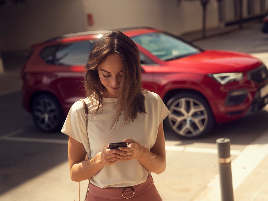 woman with smartphone using seat connect online services next to a red seat ateca.