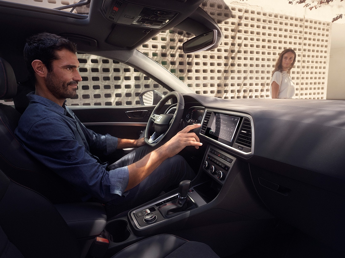 A man enjoying driving the seat ateca while a woman is watching outside.