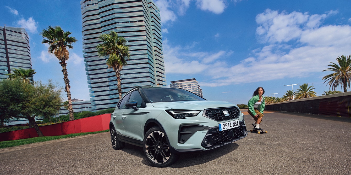 SEAT Arona parked on a sunny street with modern urban buildings and a skater passing by.