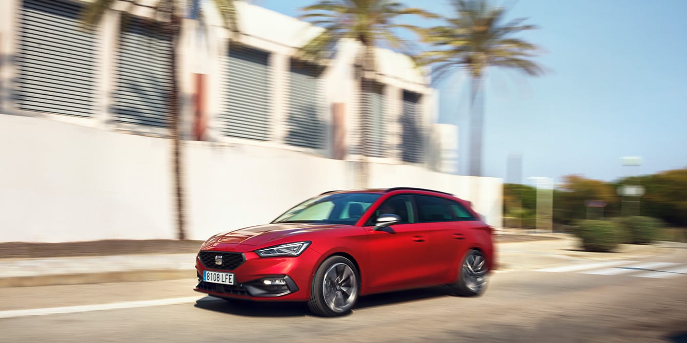 Red SEAT Leon Sportstourer in motion in a residential area with a house and palmtrees.
