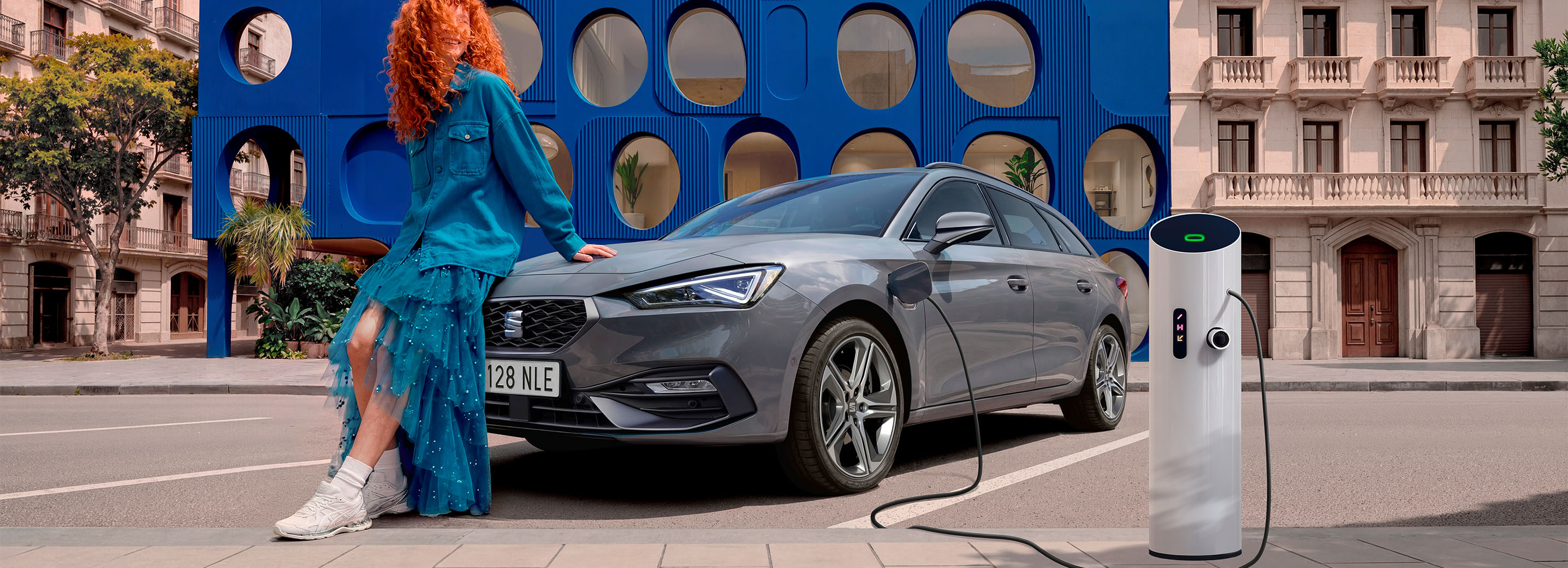 3/4 front shot of the SEAT Leon NF Sportstourer in an outdoor, urban space with buildings and a blue structure behind.