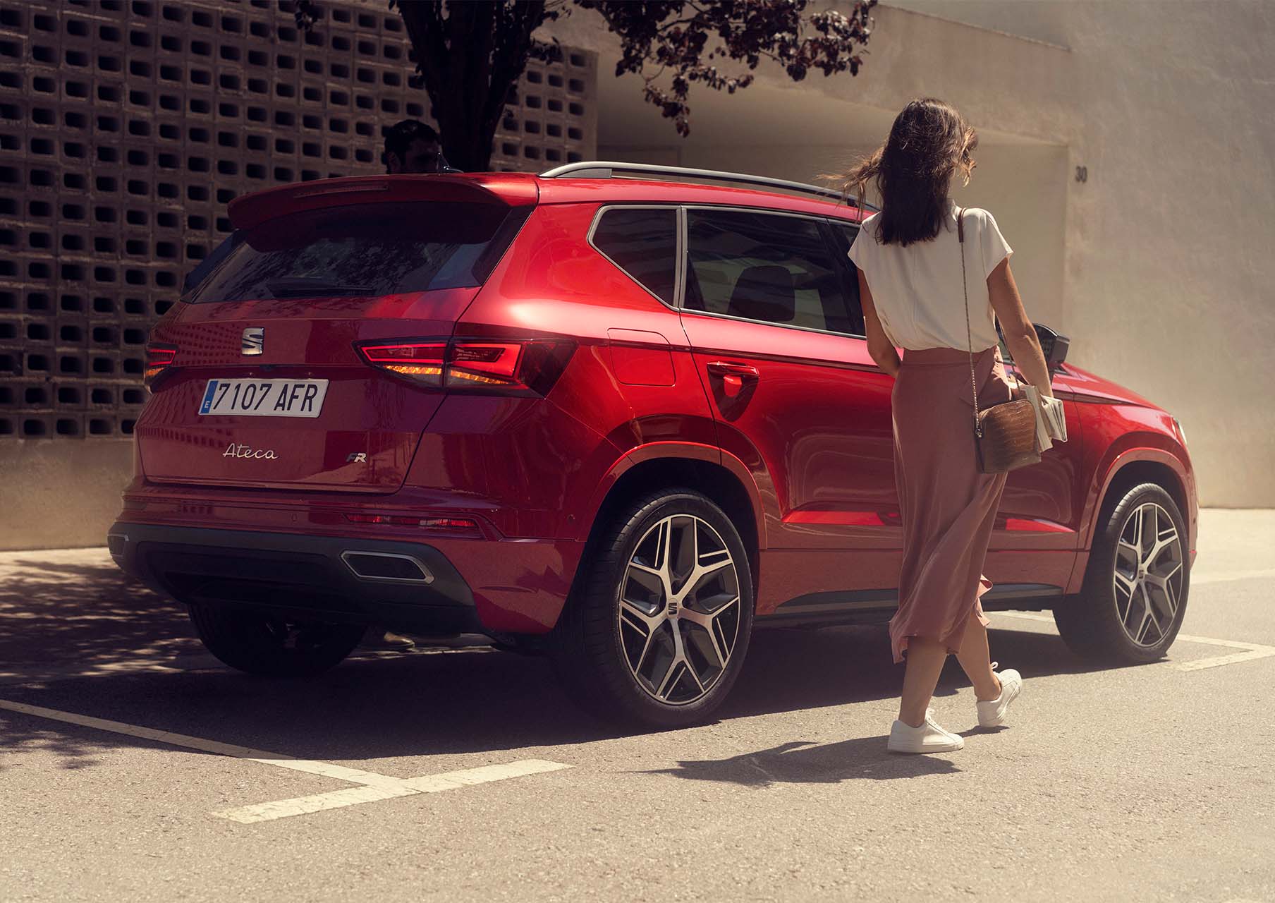 A woman walking next to a Seat Ateca in velvet red colour 