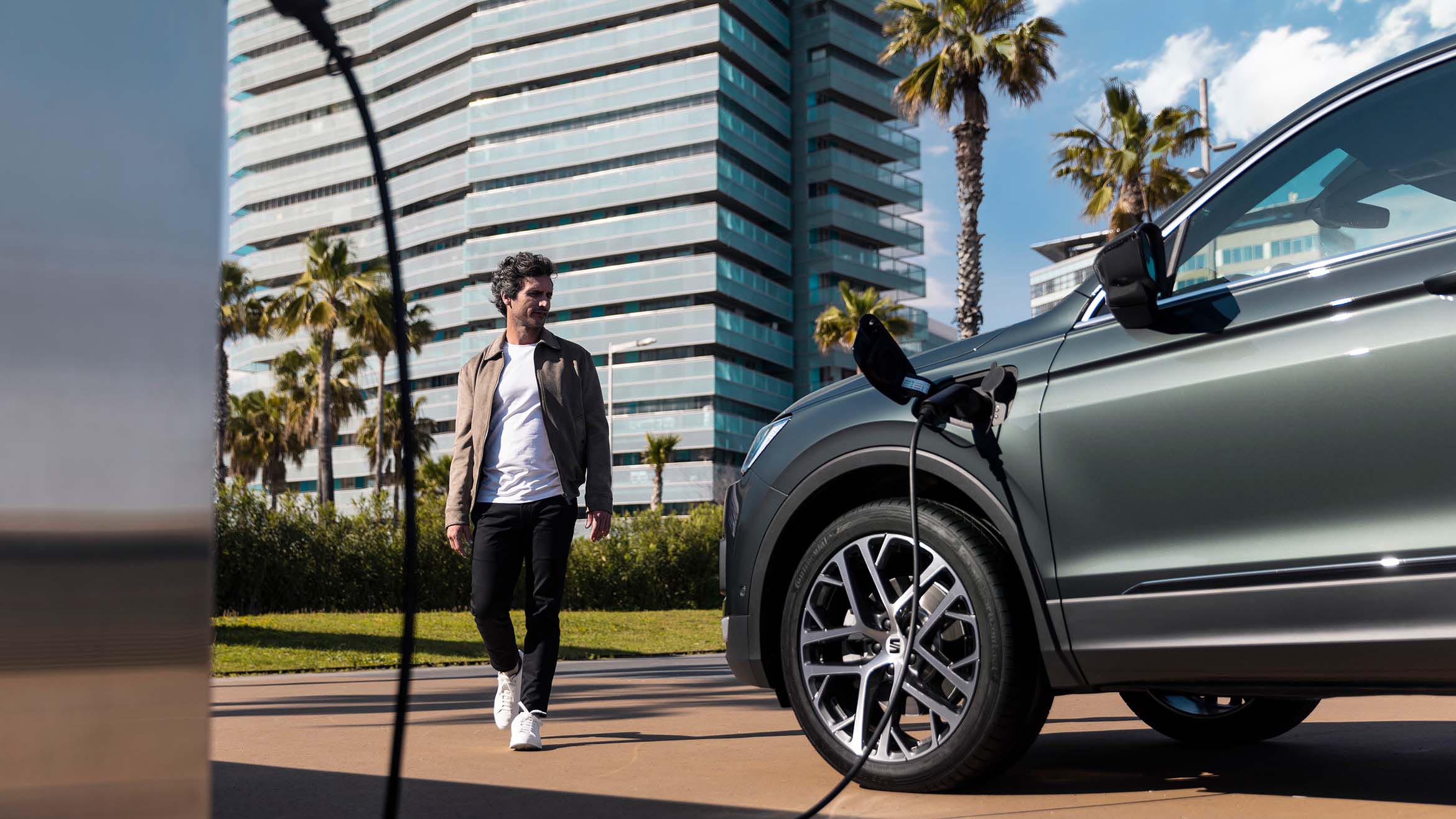 Man in front of a charging  SEAT Tarraco XPERIENCE Dark Camouflage colour with alloy wheel