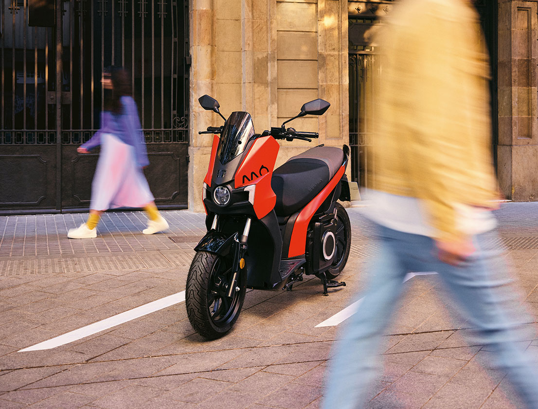 a couple walking around the parked SEAT MO 125 electric scooter