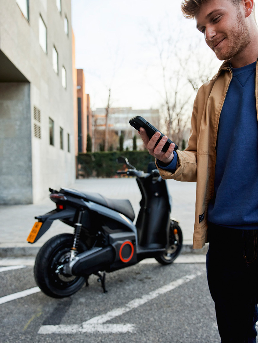 a man looking at his mobile in front of a SEAT MO 50 electric scooter