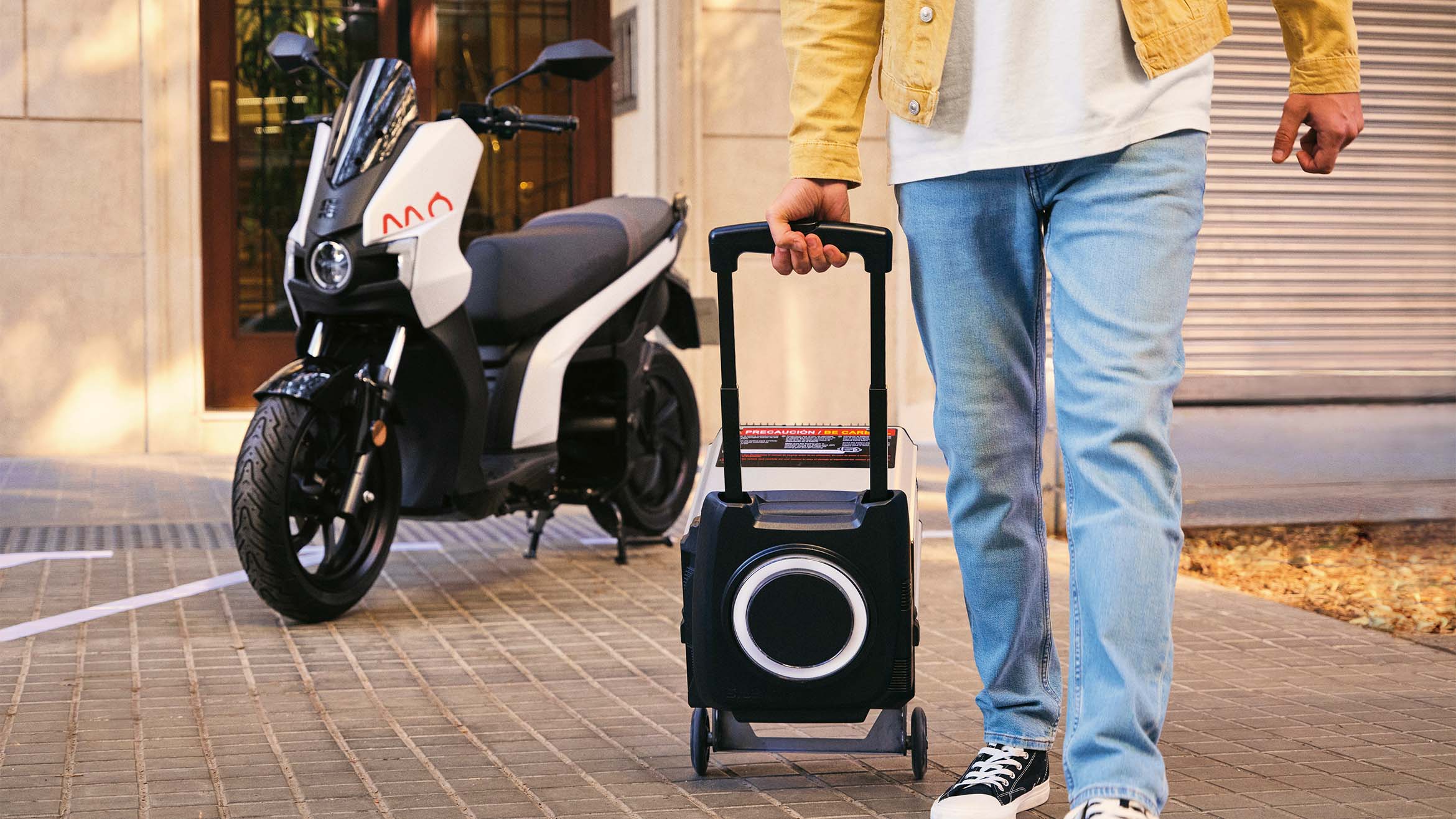 a man carrying the battery of his removable SEAT MO 125 scooter