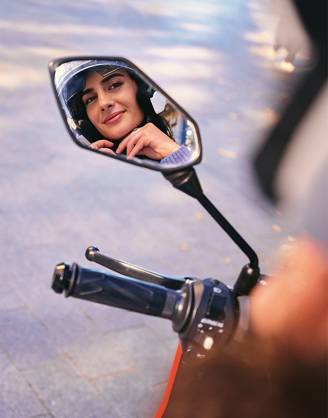 a girl looking at herself through out the rearview mirror of her scooter