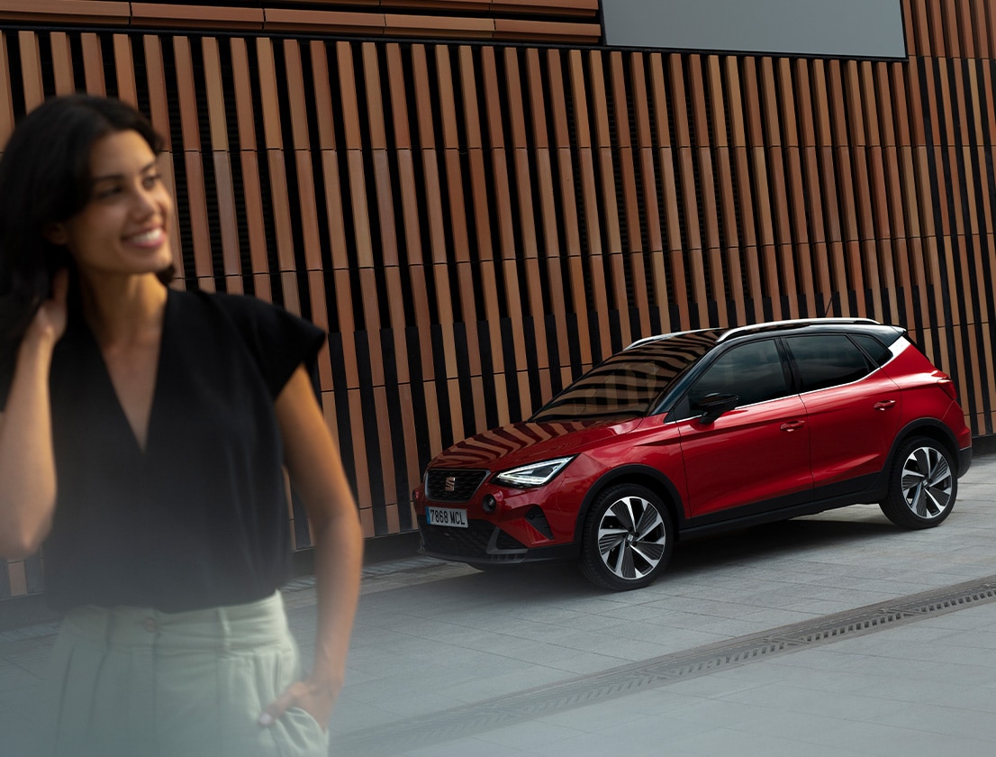 Red SEAT Arona SUV parked on a modern street with a wooden-panelled wall in the background