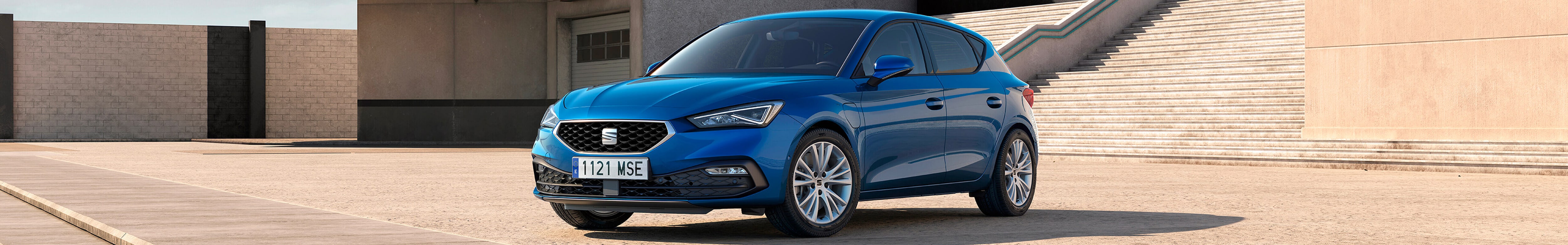 A blue SEAT Leon hatchback parked on a concrete surface in front of a modernist building with wide stairs and clear skies.
