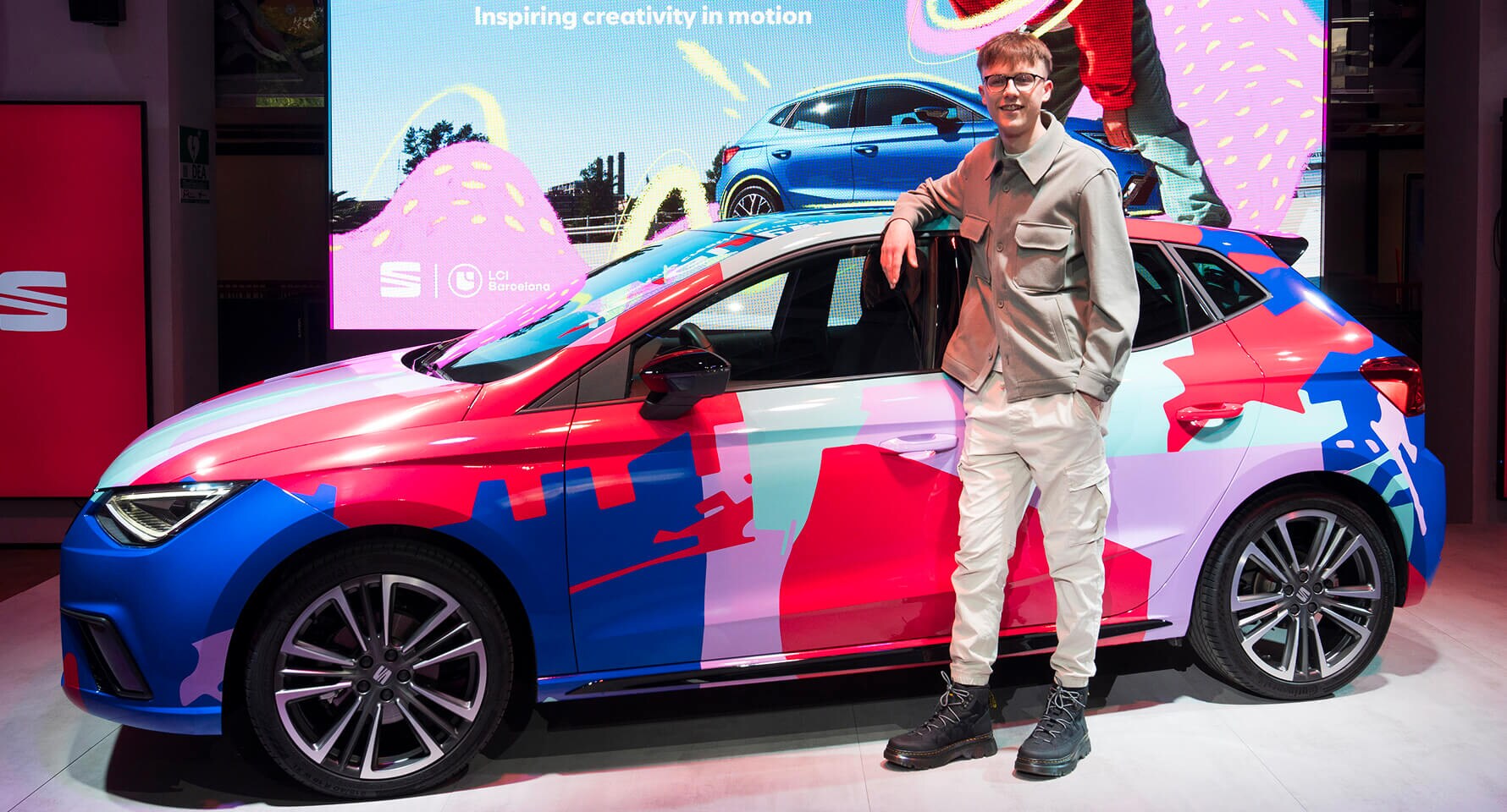 Jamie Binstead beside his SEAT Ibiza design, featuring a vibrant collage inspired by Barcelona’s skyline. The artwork marks SEAT’s 75th anniversary and celebrates its creative legacy.