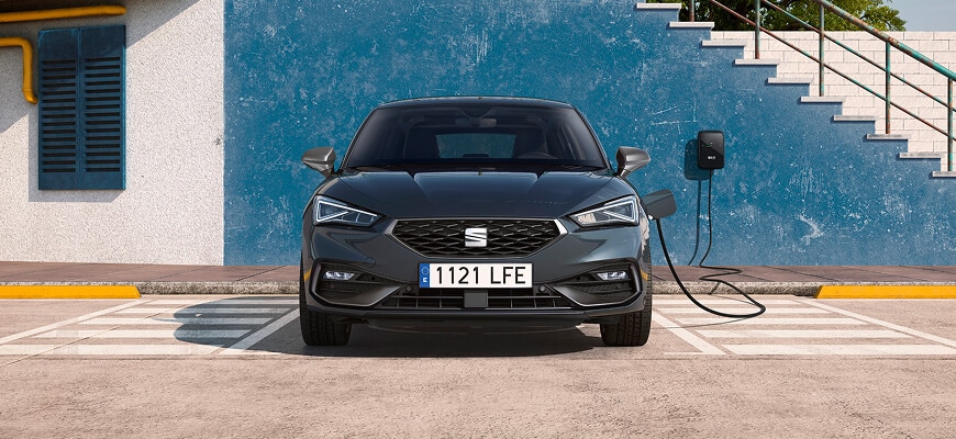 Front view of a SEAT Leon plug-in hybrid parked in front of a blue wall, connected to a Wallbox charger.