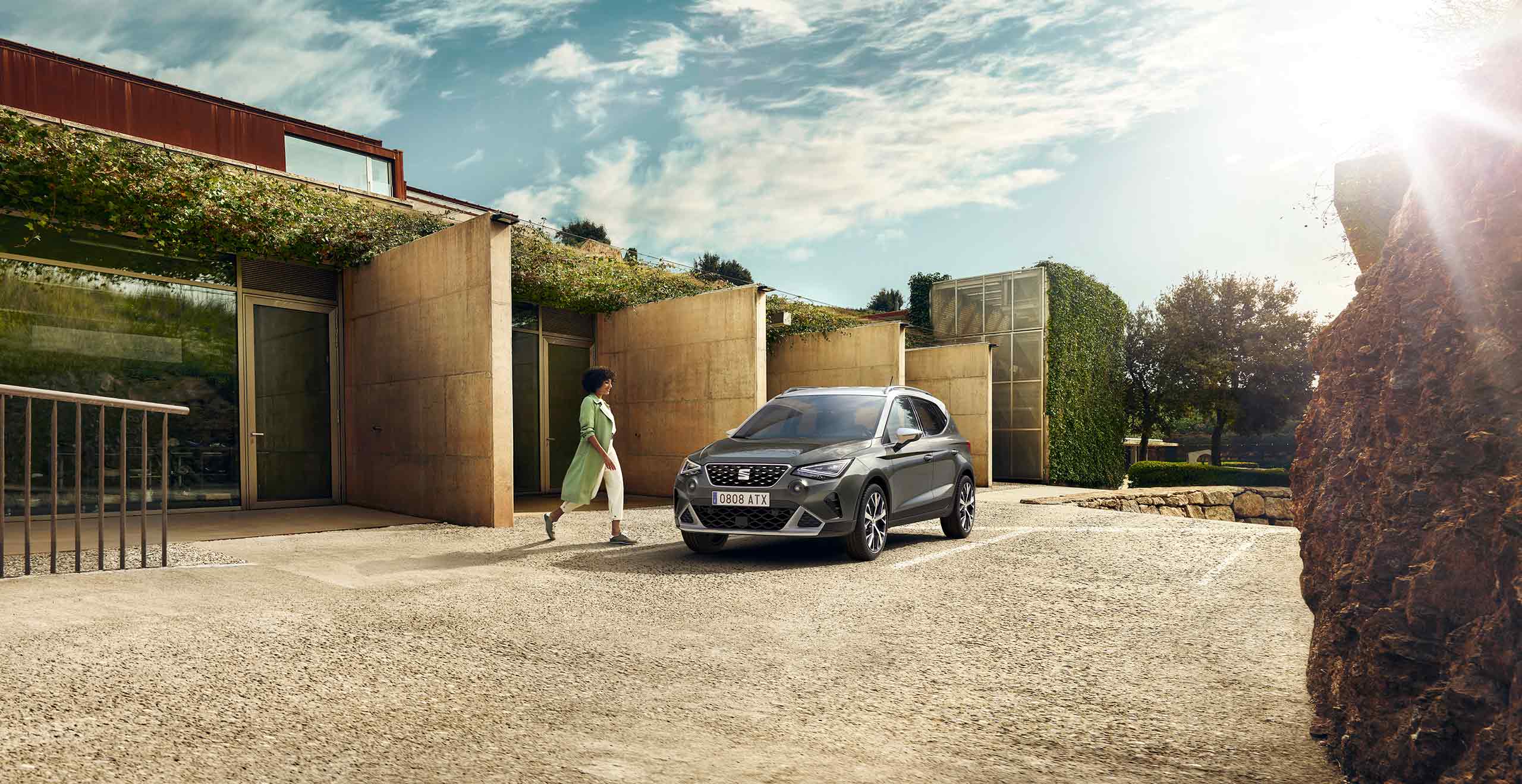 Woman walking to SEAT Arona dark camouflage colour with a candy white roof. 