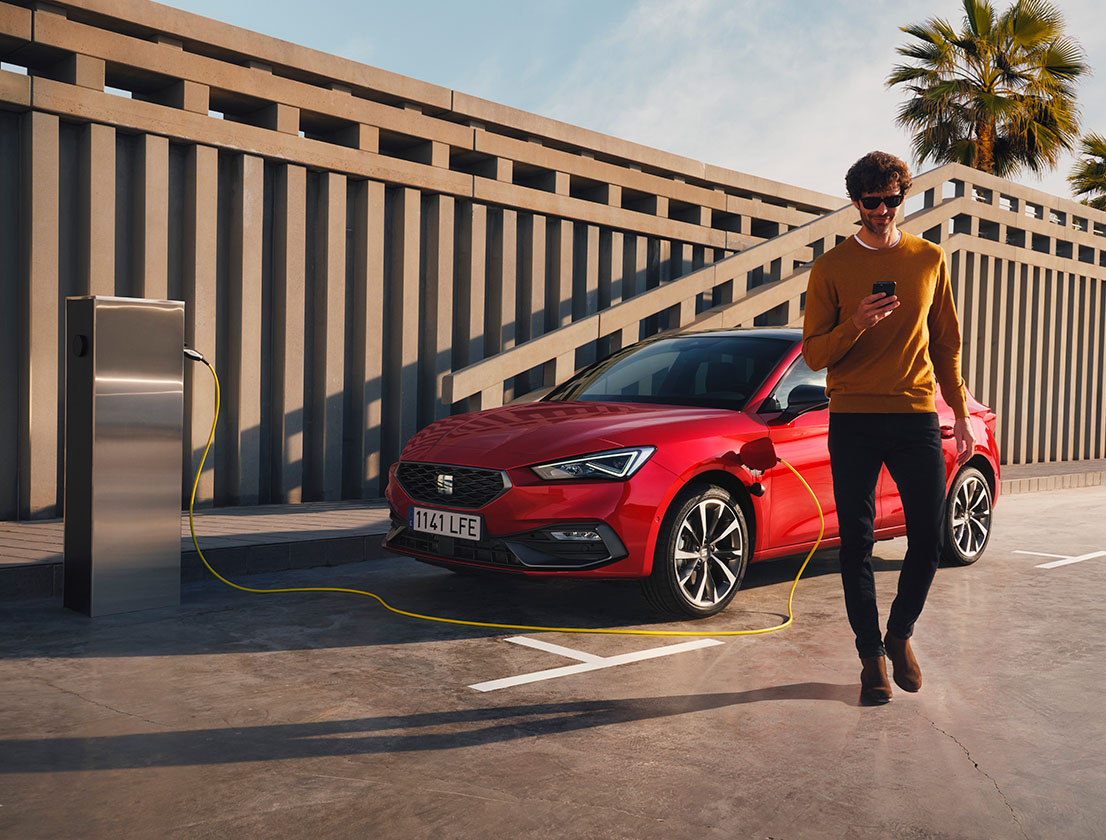 man walking away from the seat leon e-hybrid desire red colour using his smartphone