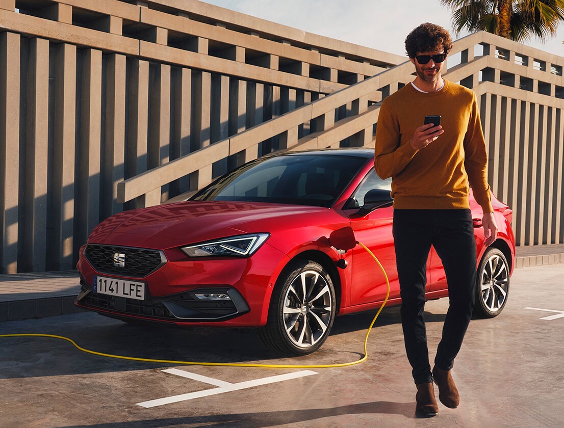 man walking away from the seat leon e-hybrid desire red colour using his smartphone