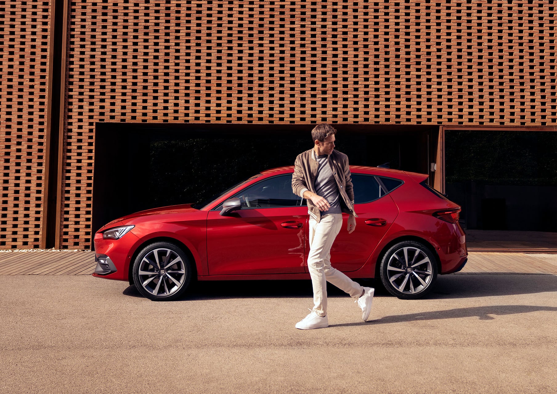 man walking next to seat leon desire red colour with alloy wheels  