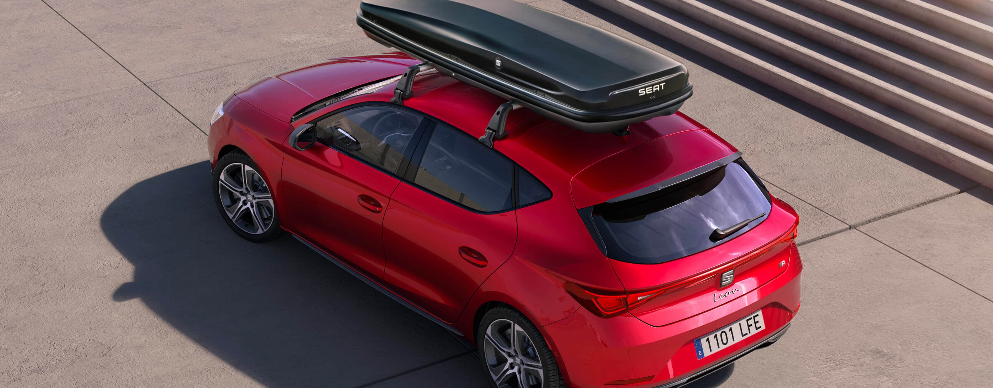A SEAT Leon in Desire Red with a roof box is parked on a concrete surface next to a staircase.