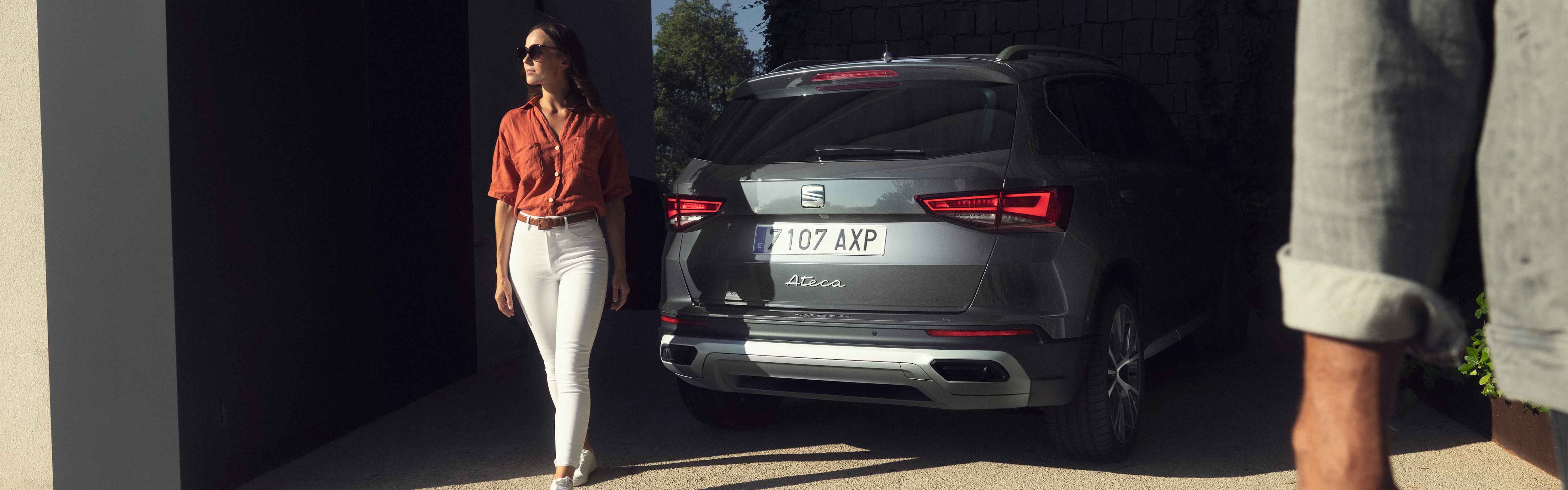 A woman standing next to a SEAT Ateca in graphite grey colour with full rear lead lights