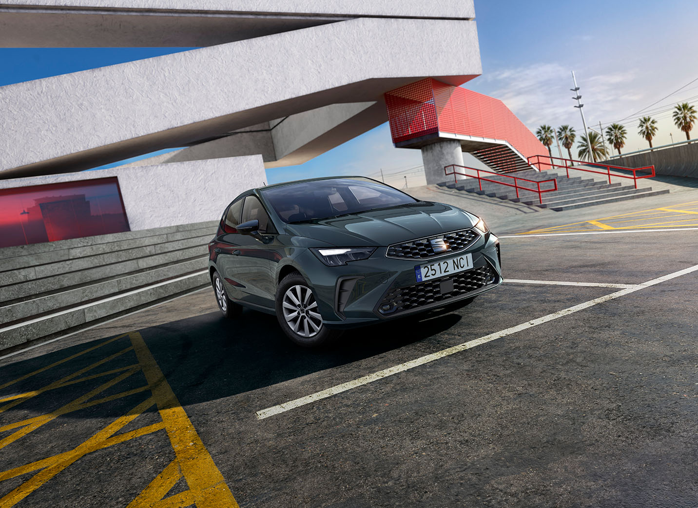 A SEAT Ibiza is parked in an asphalt lot with yellow and white markings. In the background is a striking, modern building with sharp angles in white and red, including a prominent staircase.