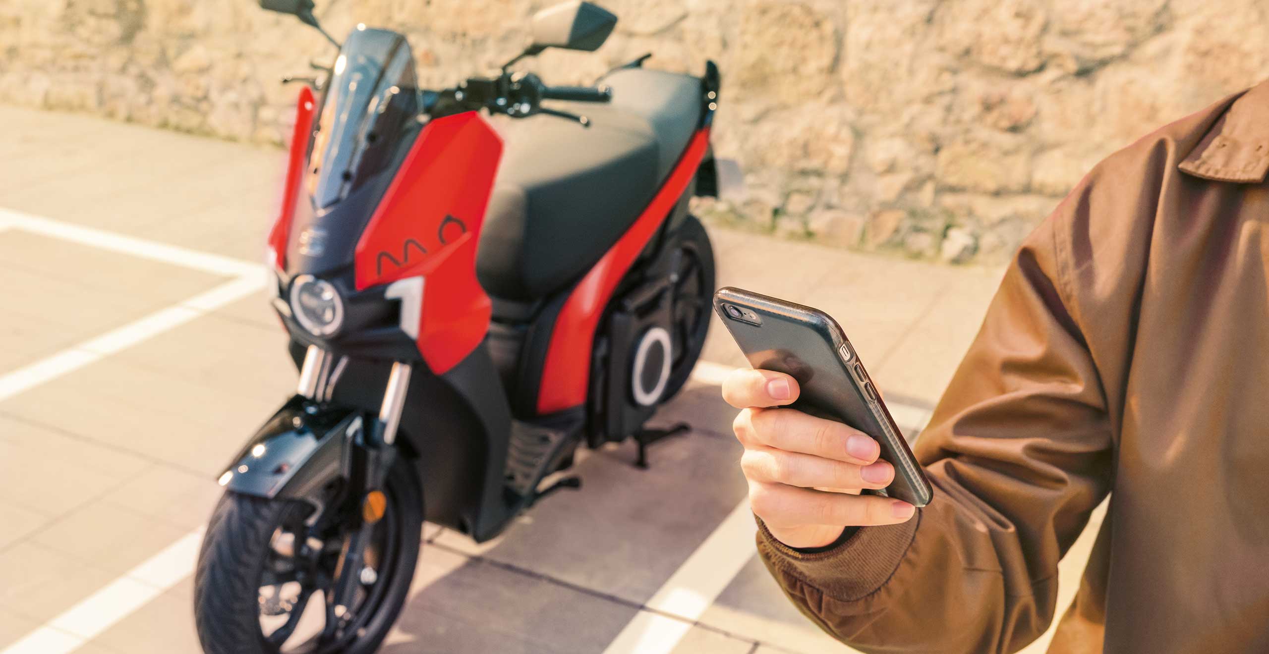 man holding a cell phone next to a seat mo 125 electric scooter